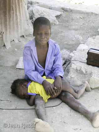 Haitian boy watches baby sister while mom works